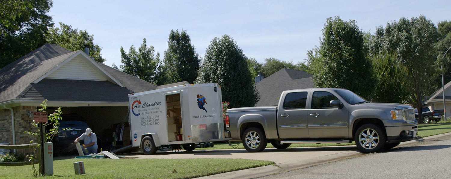 An Air Chandler van and trailer parked beside a pickup in a Tyler-area neighborhood
