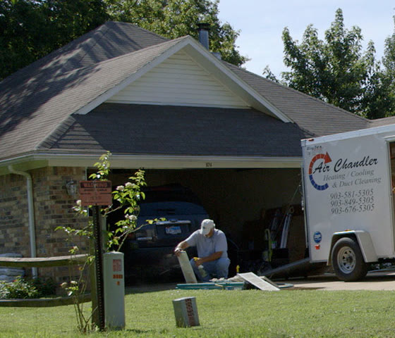 A technician kneeling at a house with an Air Chandler trailer in the driveway